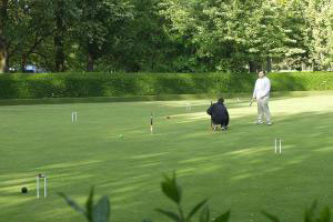 People playing croquet on a beutifully cut lawn.